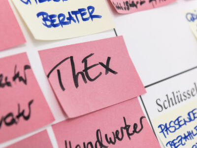 An einem Whiteboard hängen zahlreiche Post-it-Zettel. Darunter ein Zettel mit der Aufschrift ThEx.