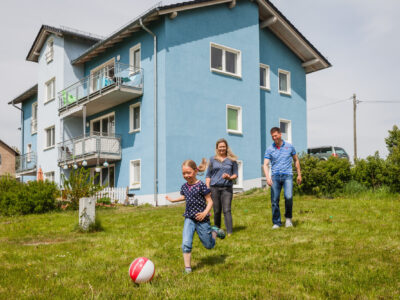 Wohneigentum für Familien Eine Familie spielt Fußball im Garten des eigenen Hauses.