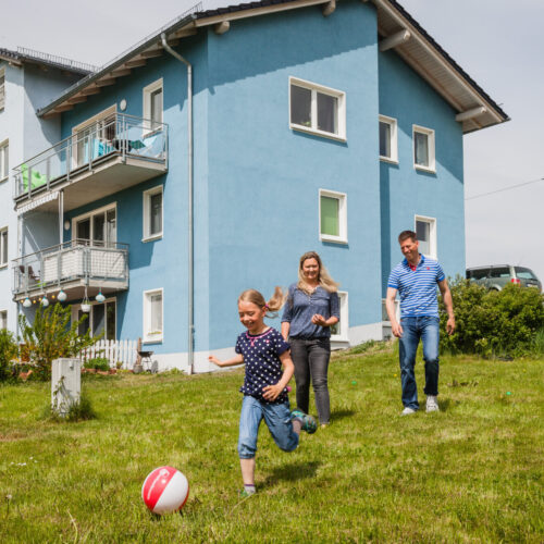 Eine Familie spielt Fußball im Garten des eigenen Hauses.