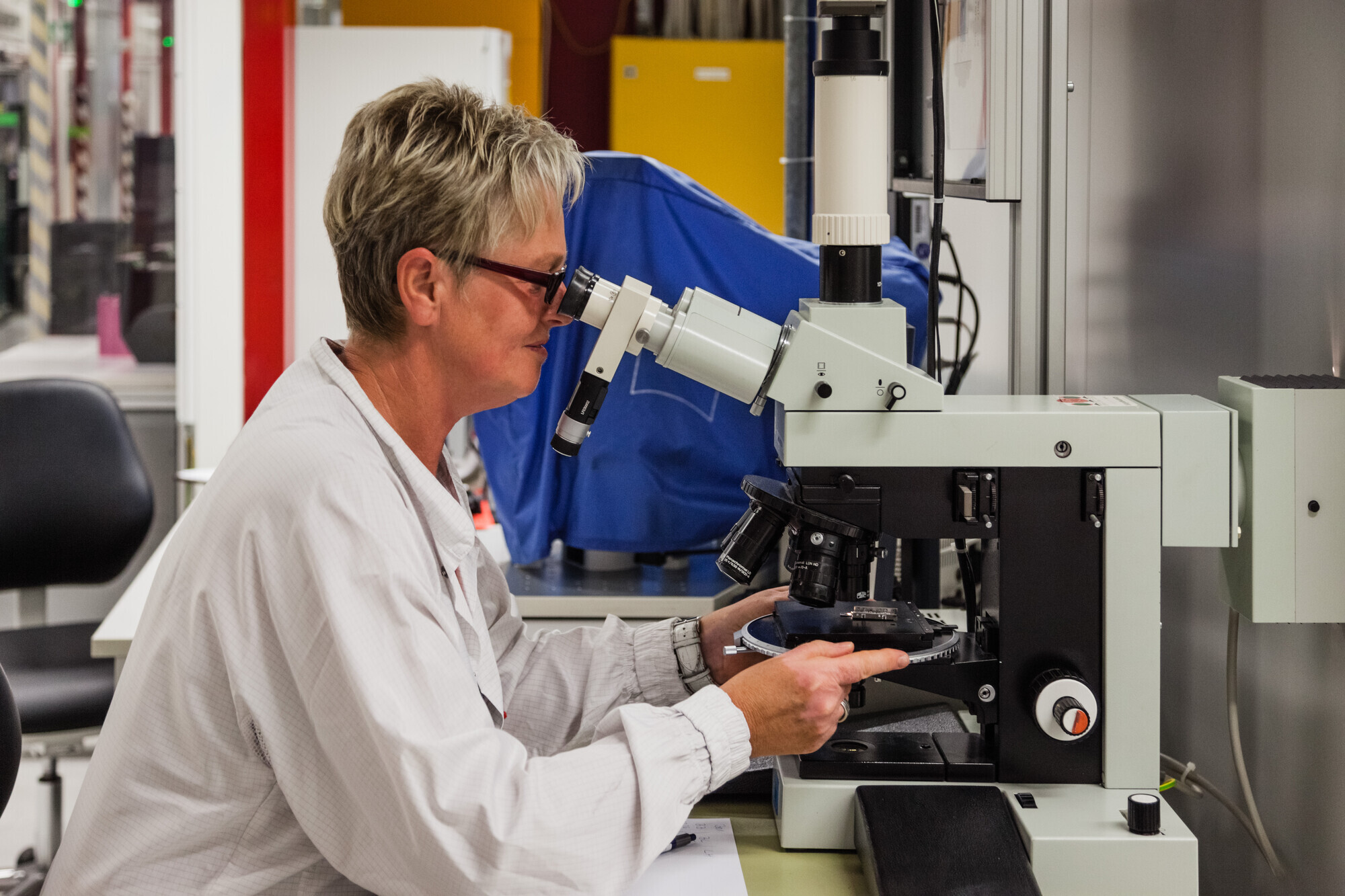 Eine Laborantin guckt durch ein Mikroskop, um eine Probe zu analysieren.