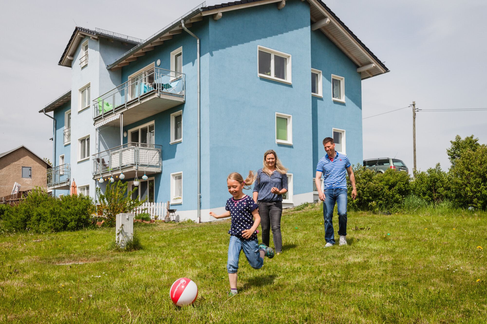 Eine Familie spielt Fußball im Garten des eigenen Hauses.