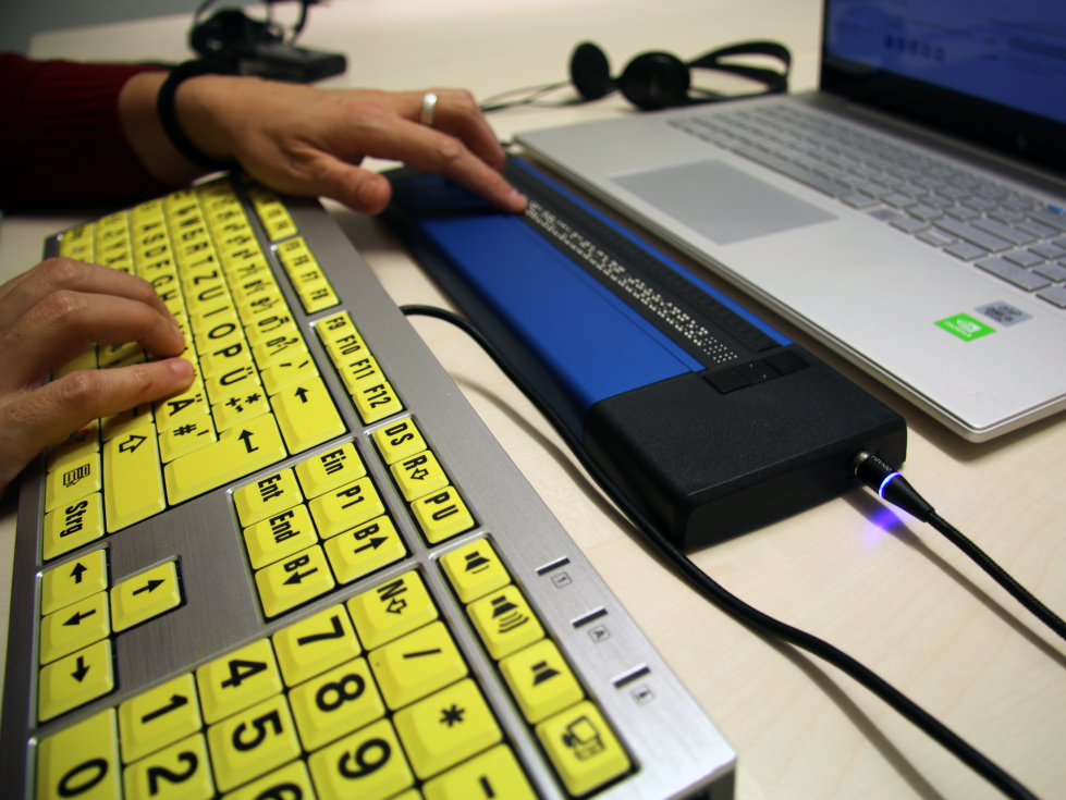 Zwei Hände bedienen eine PC-Tastatur und navigieren auf der Braillezeile.