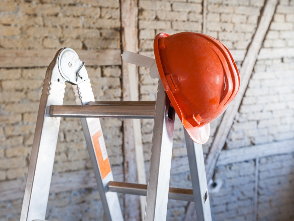 Im Bild: Eine Leiter, auf welcher ein orangener Helm hängt.