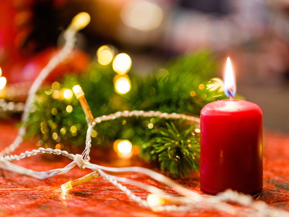 Hilfen für abgesagte Weihnachtsmärkte (im Bild: eine rote Kerze, Lichterkette und Tannengrün)