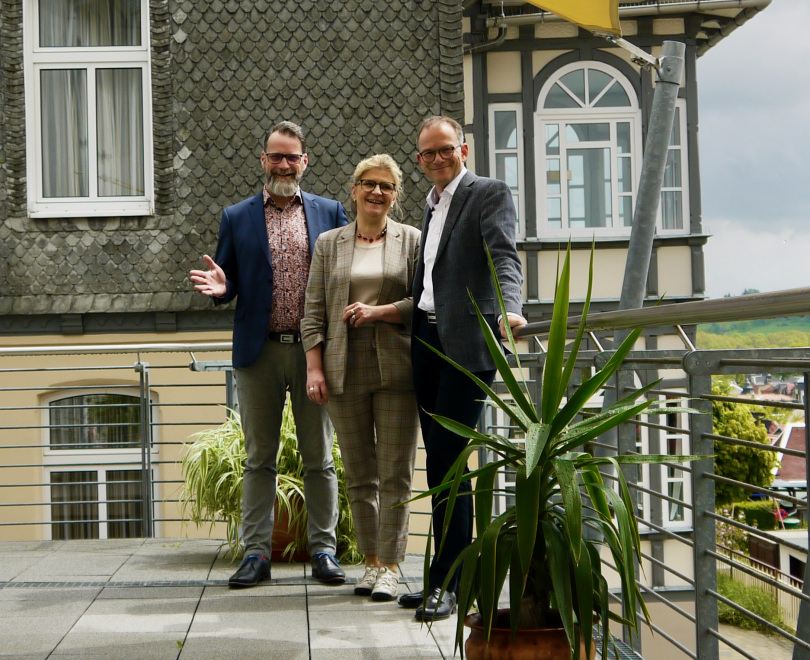 #Zuversicht: Villa Frieden (im Bild: auf der Terrasse des Allianzhaus-Cafés, im Hintergrund Villa Frieden, von links nach rechts Geschäftsführer Dr. Reinhardt Schink; Hausleiterin Gabriele Fischer-Schlüter; Marketingleiter Matthias Creutzberg)