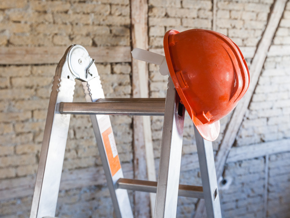 Im Bild: Eine Leiter, auf welcher ein orangener Helm hängt.
